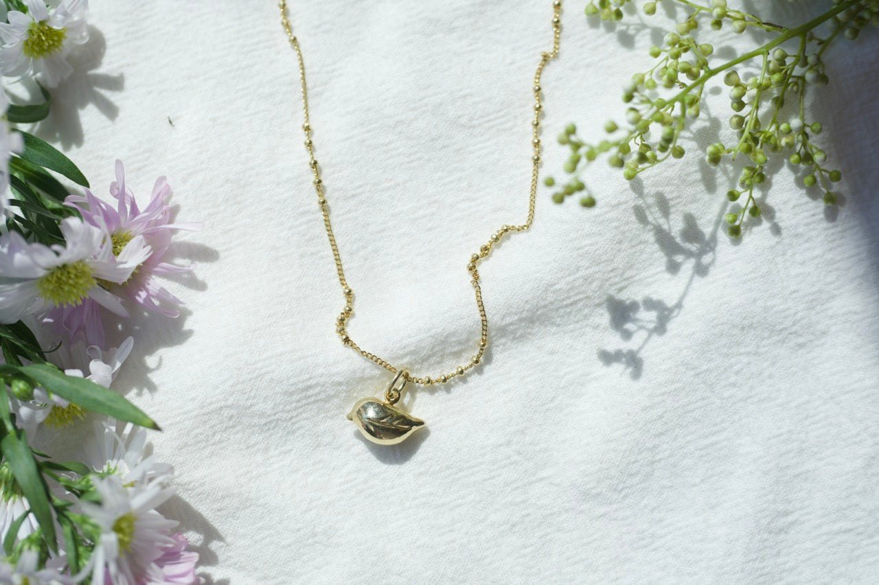 sparrow bird necklaced displayed on cloth beside flowers